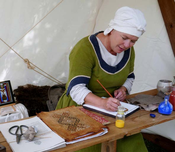Kvinde i grønt middelaldertøj udfører håndarbejde på et træbord, på Middelaldermarked i Skælskør