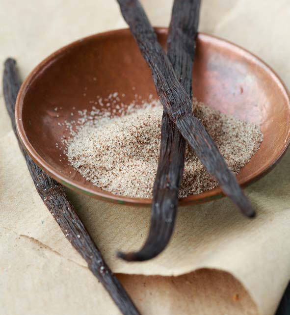 3 vaniljestænger ligger ved en brun skål der er indeholder vaniljesukker