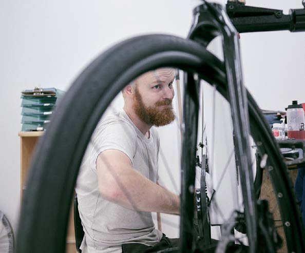 Mand i hvid t-shirt sidder og arbejder på en sort cykel